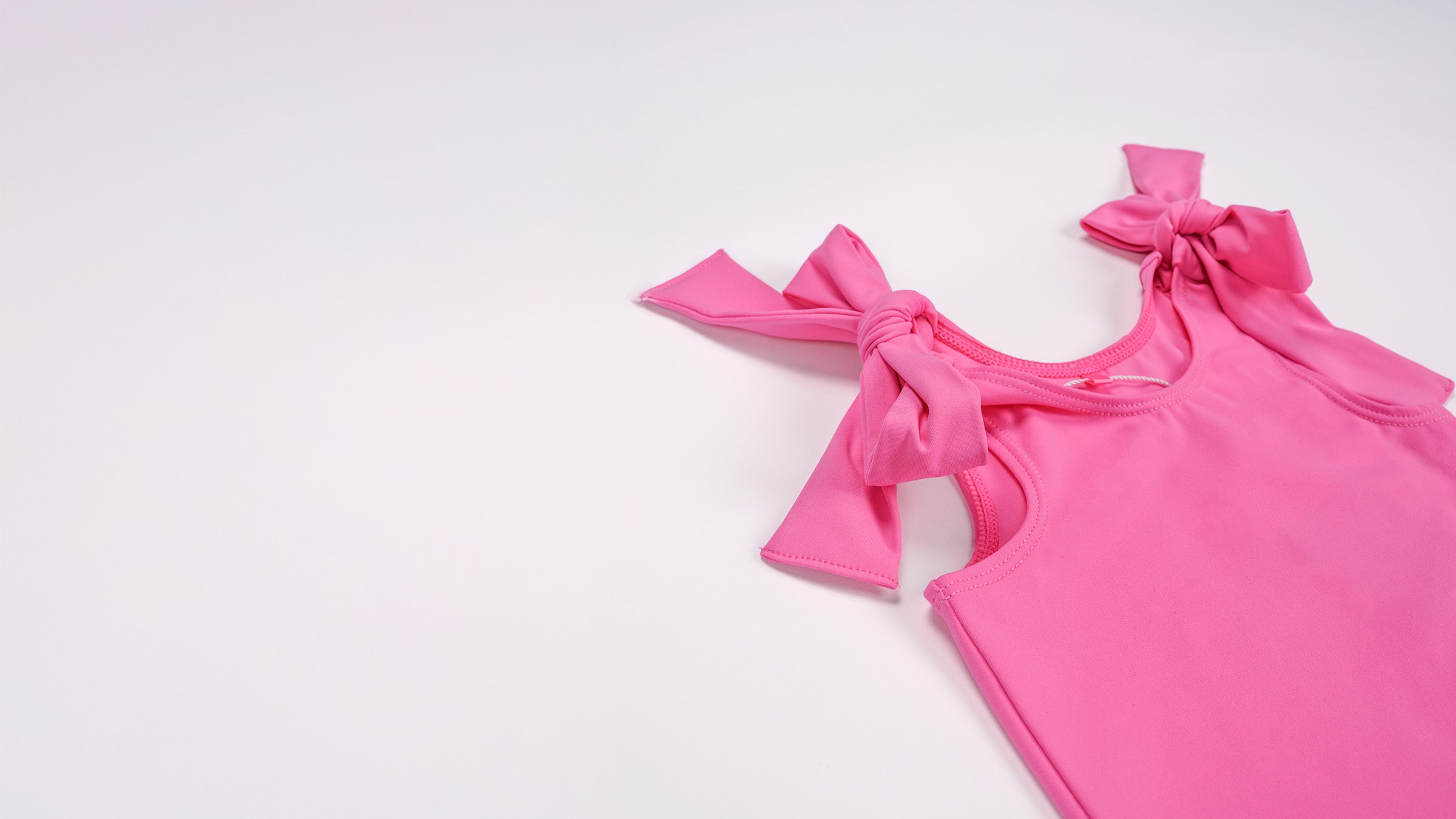 Close-up of the hot pink bow shoulder detail on a baby bodysuit, showcasing the Motchluxe fabric.