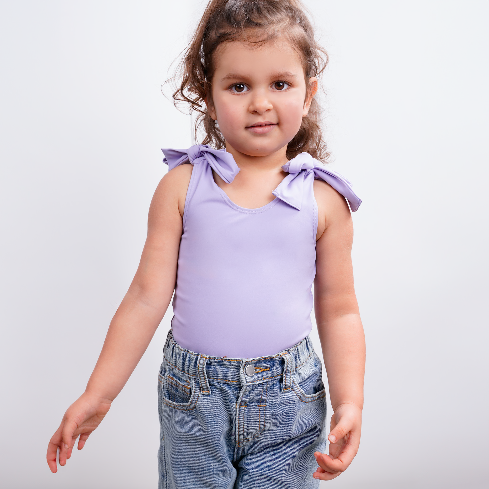 Toddler wearing Motch lavender bow shoulder bodysuit standing in front of a gray background with a slight smile