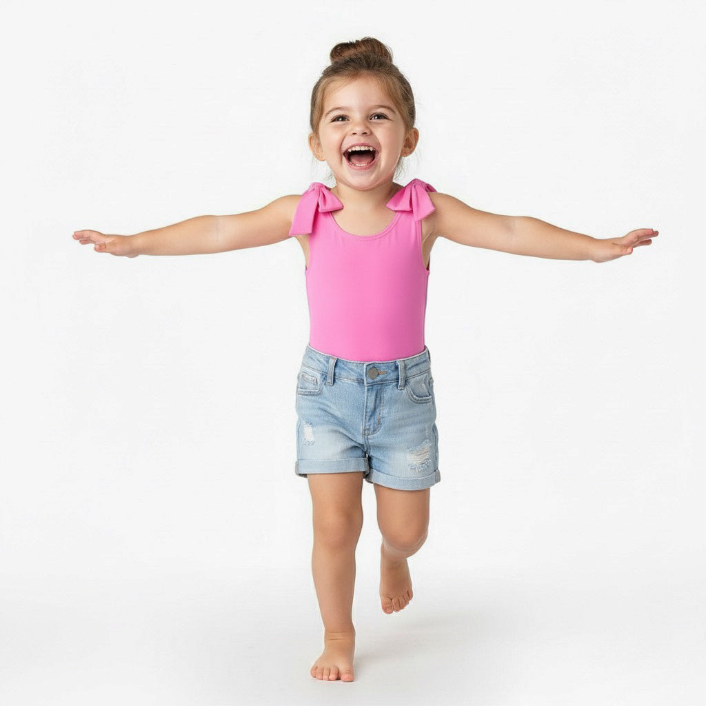 Toddler running with arms out in a Motch Hot Pink bow-shoulder bodysuit and denim shorts — a joyful, playful moment from the matching mommy-and-me collection that celebrates movement and everyday connection.