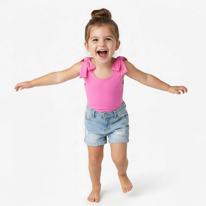 Toddler laughing and jumping in a Motch Hot Pink bow-shoulder bodysuit and denim shorts — a fun, carefree look from the matching mommy-and-me collection designed for play and everyday comfort.