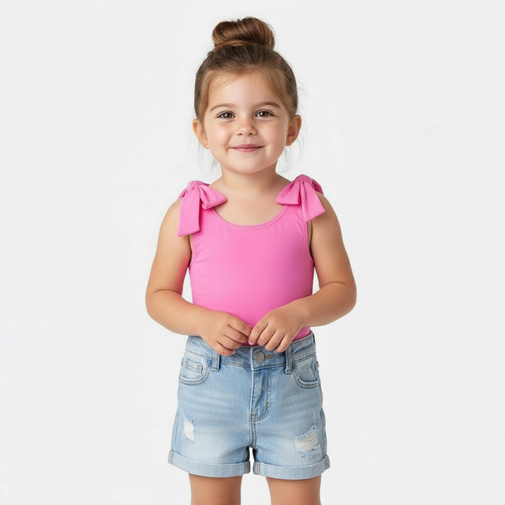 Toddler smiling in a Motch Hot Pink bow-shoulder bodysuit and denim shorts — a playful everyday look from the matching mommy-and-me collection, made for comfort and connection.