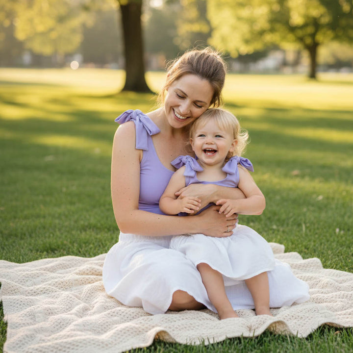 Woman and child in matching purple outfits sitting on a blanket in a park