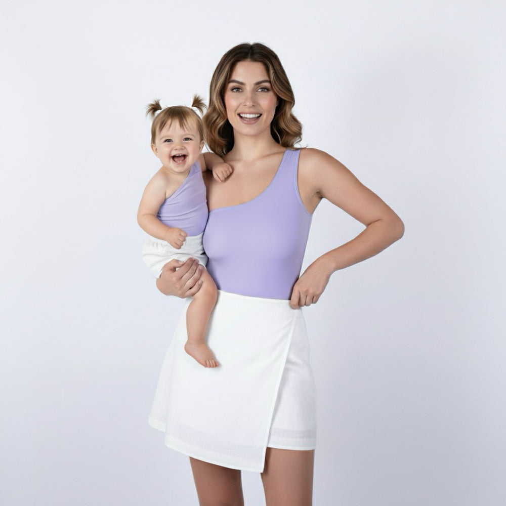 Mom and baby smiling in matching lavender one-shoulder Motch bodysuits with white skirts — a joyful, coordinated look that captures effortless mommy-and-me style in soft pastels.