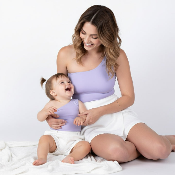 Mom and baby smiling in matching lavender one-shoulder Motch bodysuits with white skirts — a sweet mommy-and-me look that blends comfort, connection, and modern minimalism.