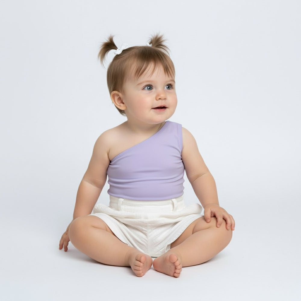 Baby sitting in a lavender Motch one-shoulder bodysuit with white shorts — a soft, modern take on baby basics designed for comfort and matching moments with mom.
