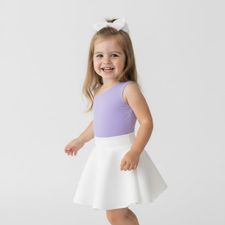 Toddler twirling in a Motch Lavender one-shoulder bodysuit and white skirt — part of the matching mommy-and-me collection celebrating movement, comfort, and everyday joy.