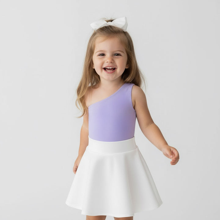 Little girl smiling in a Motch Lavender one-shoulder bodysuit and white skirt — a playful toddler look from the matching mommy-and-me collection, designed for comfort, stretch, and everyday joy.