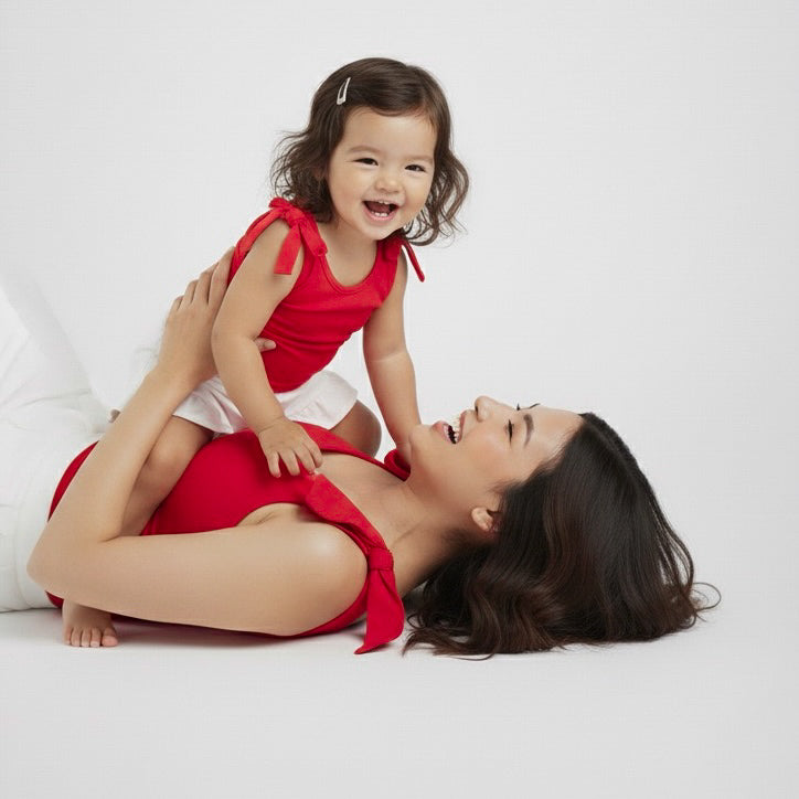 Mom and toddler wearing matching Red bow-shoulder bodysuits from Motch, laughing together while lying down, capturing the playful connection of mommy-and-me matching outfits — perfect for family photos or holiday moments.
