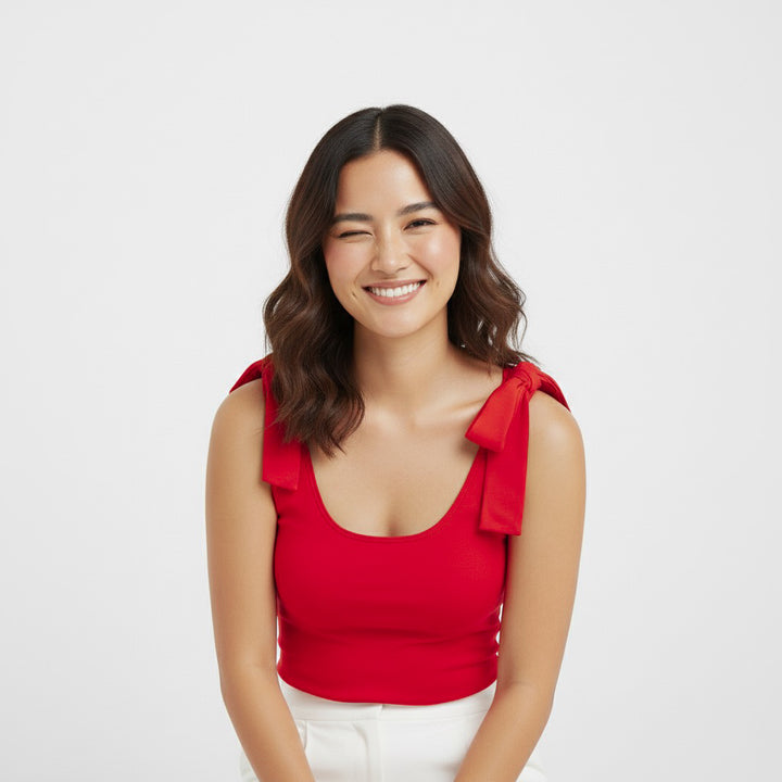 Woman smiling and winking while wearing a Red bow-shoulder bodysuit from Motch, part of a matching mommy-and-me outfit set, styled with white pants for a fun and festive look.