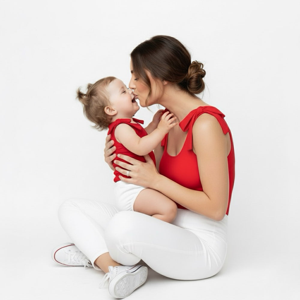Mom and baby sharing a sweet kiss in matching red Motch bow-shoulder bodysuits — a tender mommy-and-me moment full of love and connection.