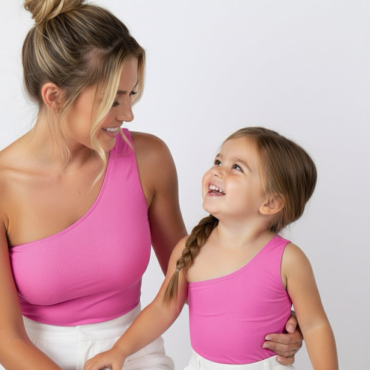 Mom and daughter smiling at each other in matching hot pink Motch one-shoulder bodysuits — joyful, connected moment.