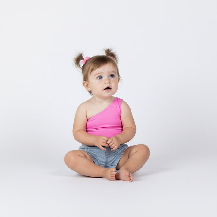 Toddler girl wearing a bright pink one-shoulder bodysuit from Motch, sitting on a white backdrop with pigtails and denim shorts, showcasing the matching mommy-and-me style.