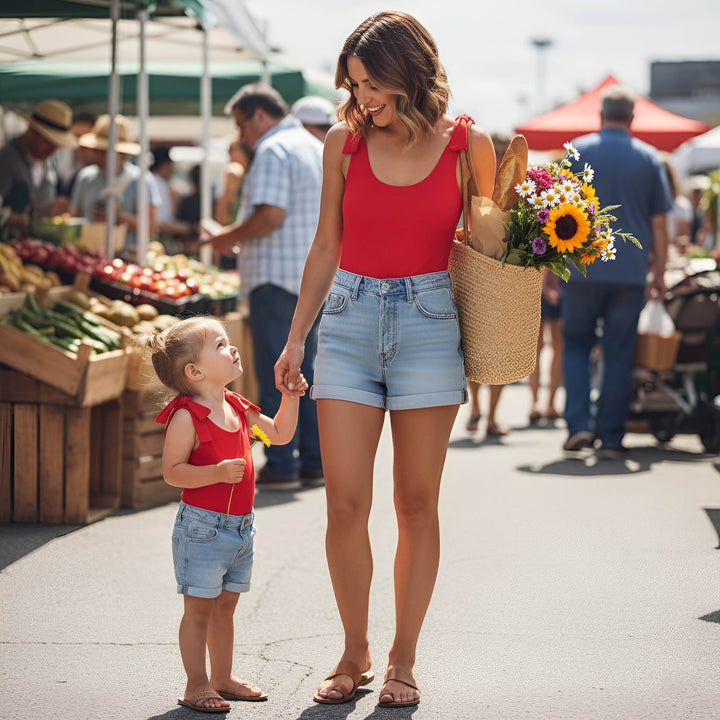 Woman and child wearing matching outfits by motch at an outdoor market holding hands with a basket of flowers.
