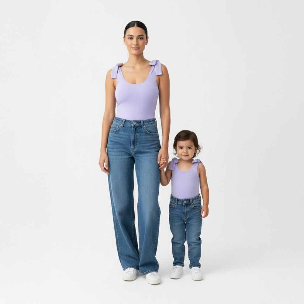 Mom and toddler wearing matching Motch Lavender bow-shoulder bodysuits with jeans, standing and holding hands — a coordinated mommy-and-me outfit that blends everyday comfort with timeless style.