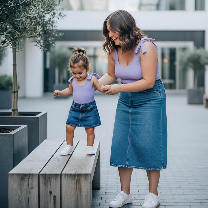 Woman and child in matching purple tops and blue skirts standing outdoors.