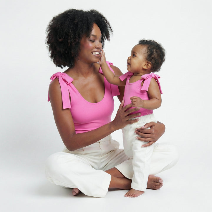 Woman and child wearing matching pink tops and white pants on a white studio background