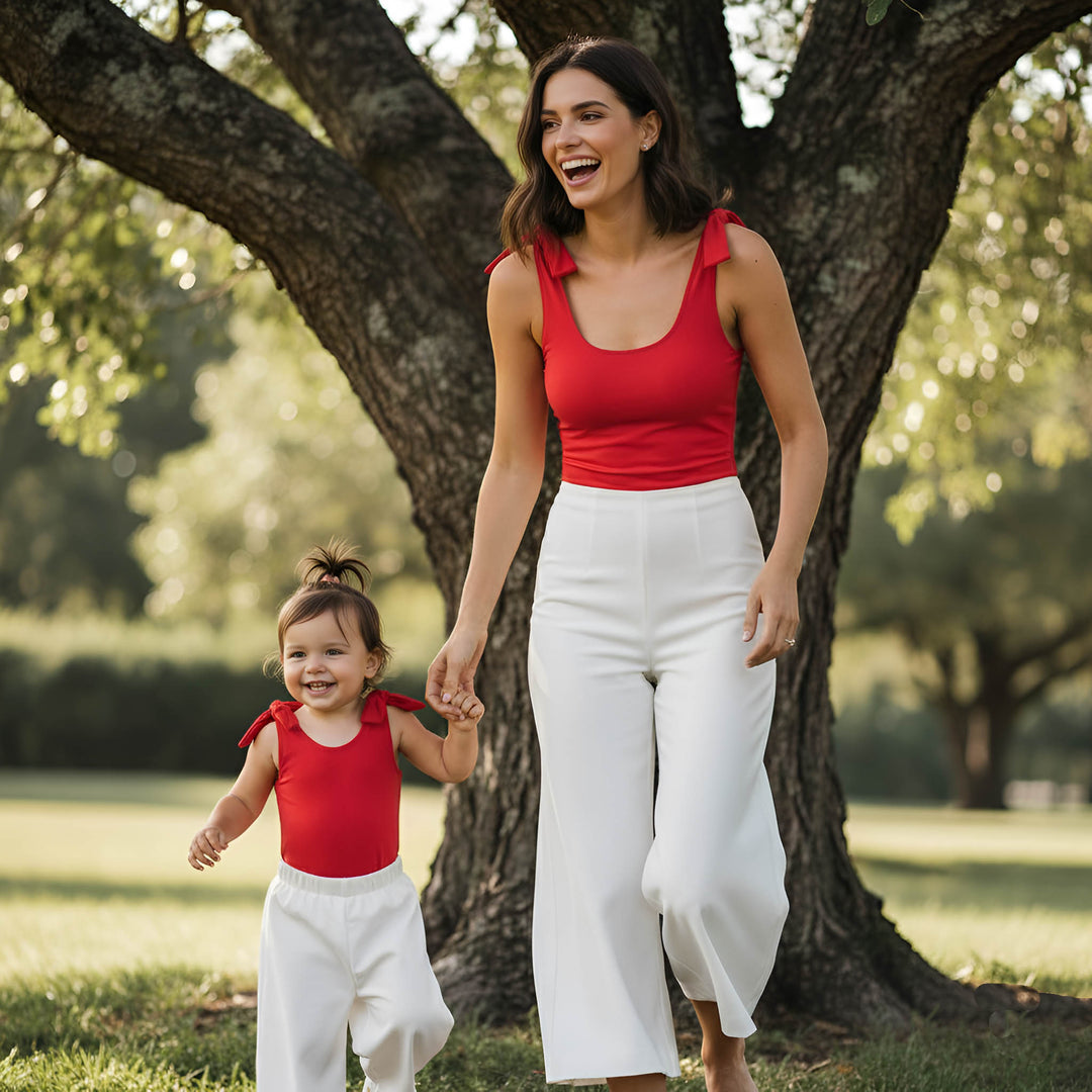 Woman and child in red tops and white pants walking together in a park.