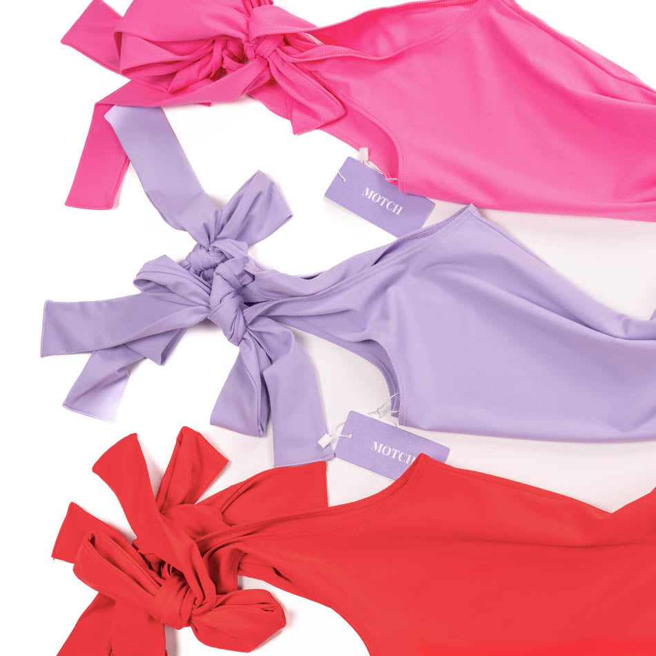 Flat lay of Motch bodysuits in pink, lavender, and red showing fabric colors