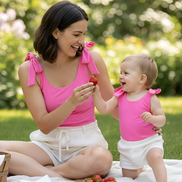 Woman and baby in matching pink tops sitting on a blanket outdoors
