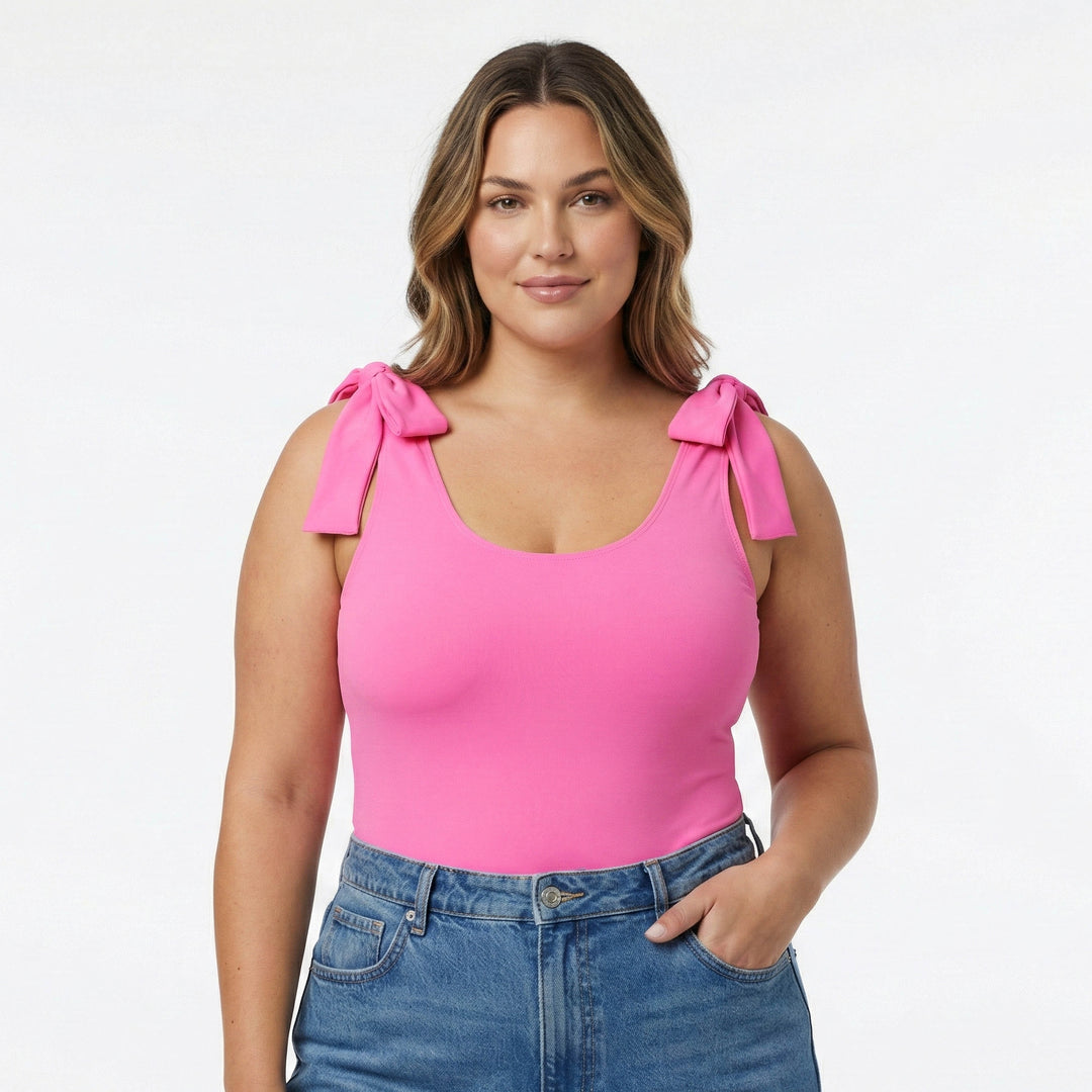 Size XL Woman wearing a pink top with bow straps and blue jeans on a white studio background