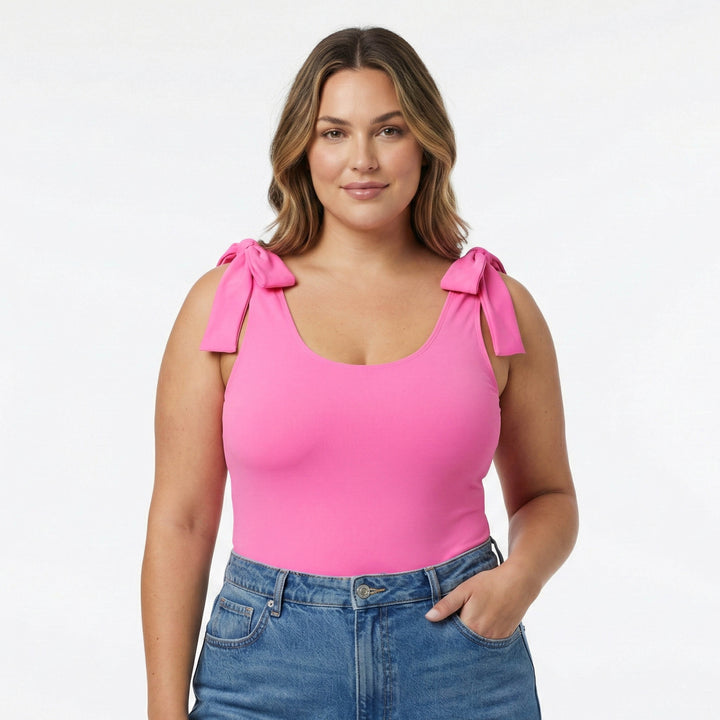 Size XL Woman wearing a pink top with bow straps and blue jeans on a white studio background